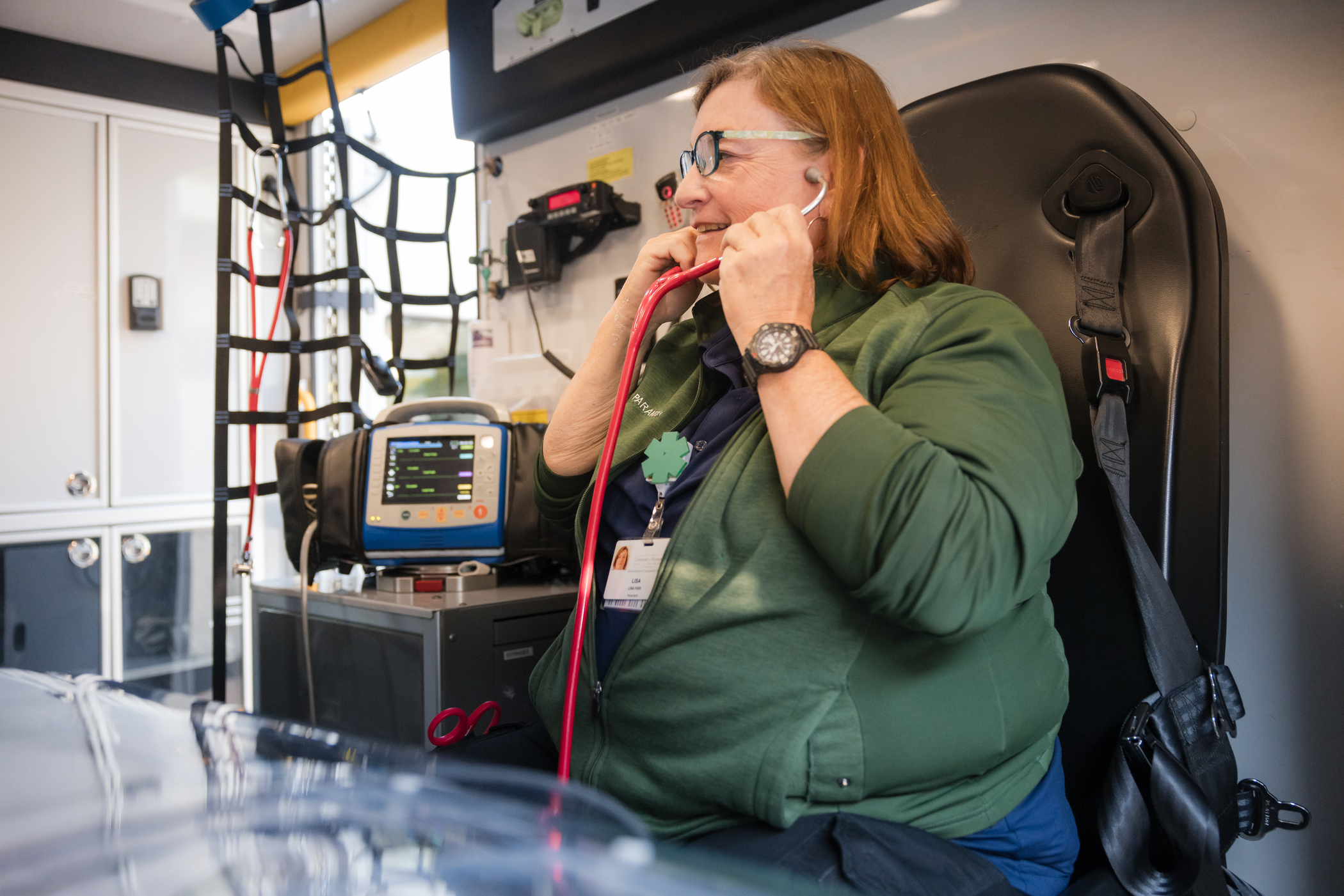 Female ECH EMT sitting in ambulance putting on stethoscope.