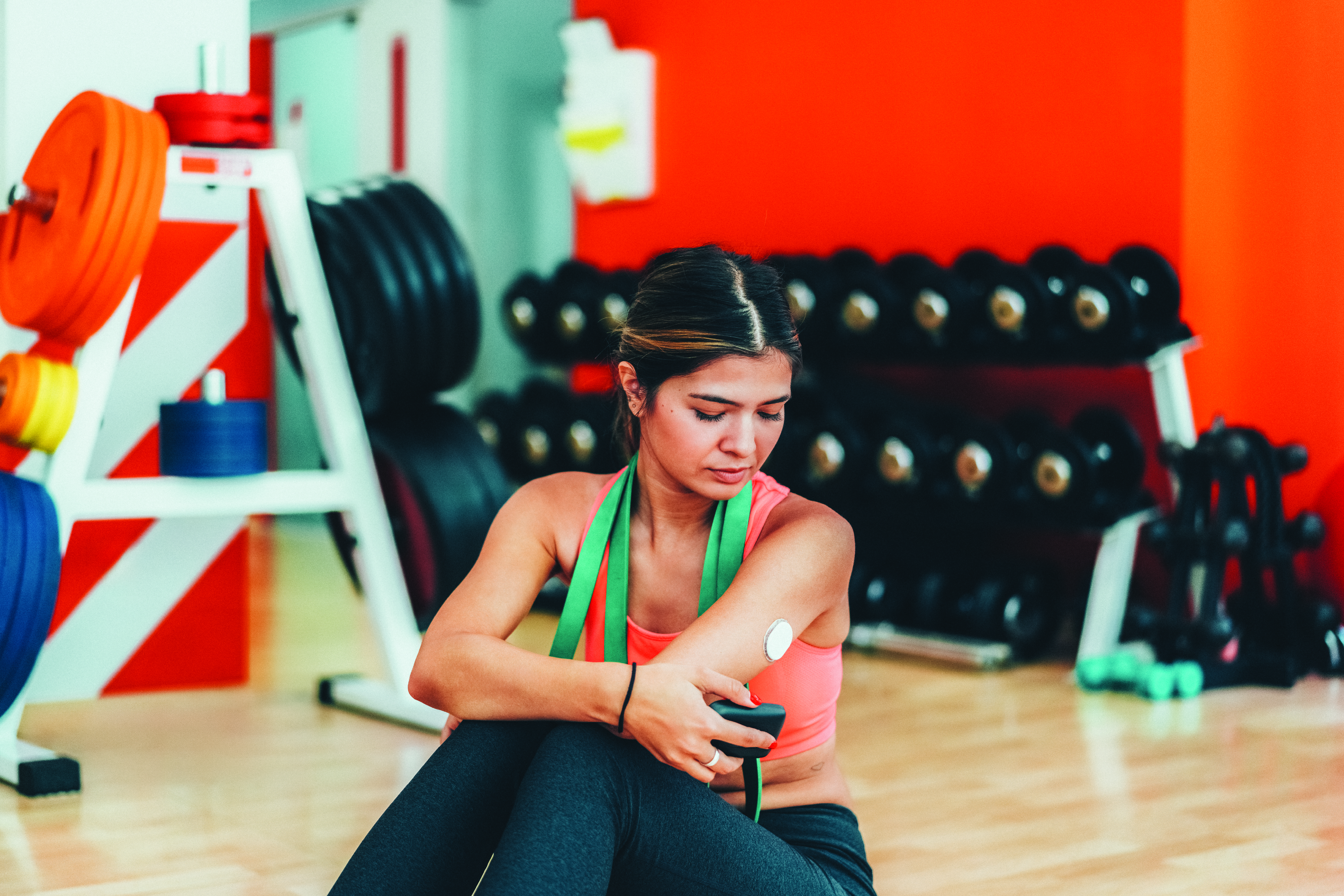 Stock photo of a woman checking her continuous glucose monitor while at the gym.