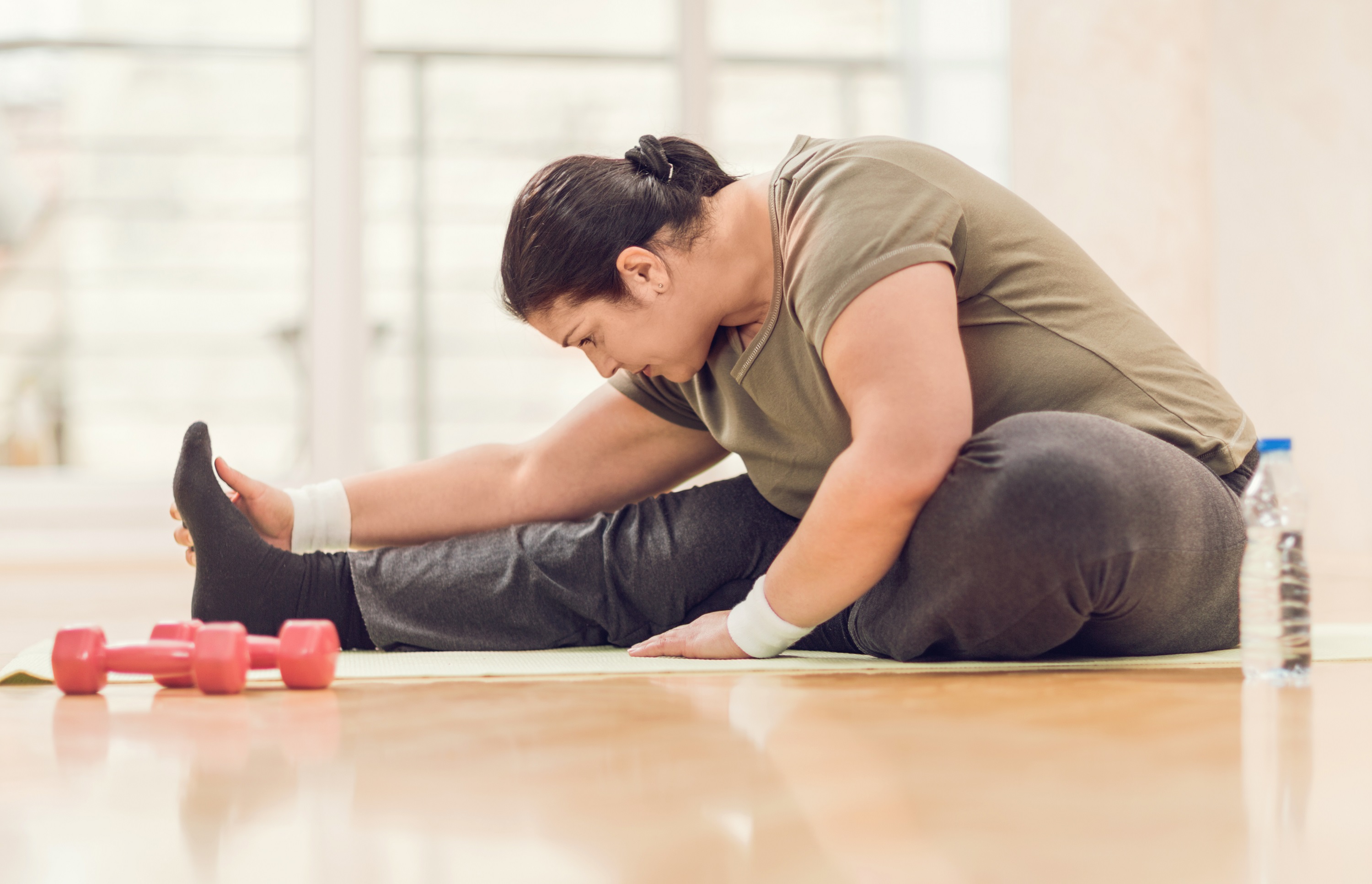 A woman stretches next to weights.