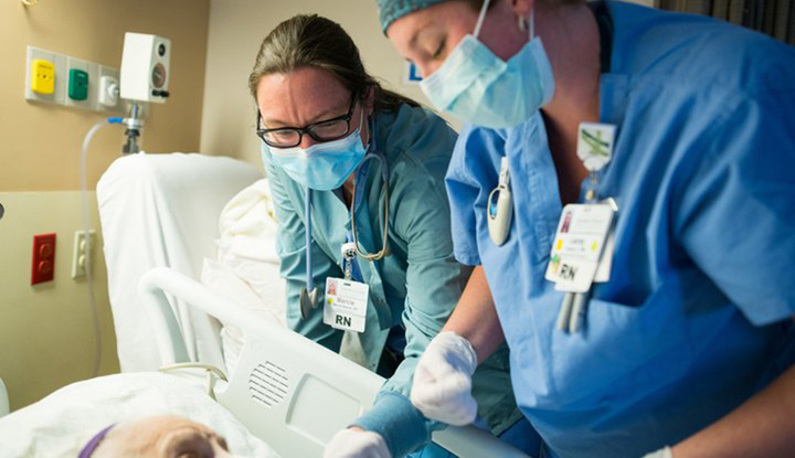 Nurses stand over a bedside.