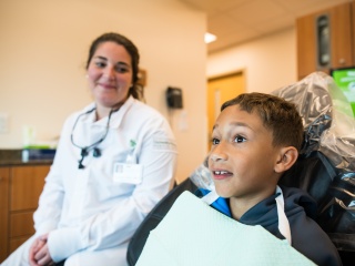 A dental specialist sits with a pediatric patient in chair.