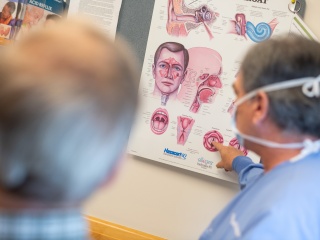 A masked doctor shows an illustration of a throat to a patient.