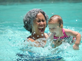 An older woman swims with a young infant in a swimming pool.