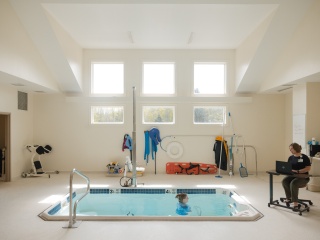 A physical therapist works with a patient who is swimming in a pool.