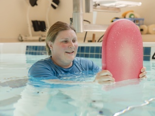 A patient holds onto a board while swimming in a pool.