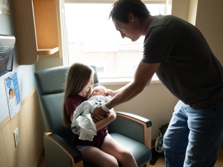 A father helps his daughter hold her newborn sibling.
