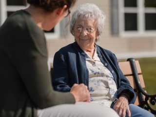 A resident of The Alice Center at Alice Hyde Medical Center chats with a staff member on a bench outdoors.