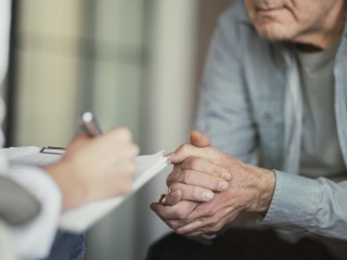 Adult man holding his hands while seating and talking with therapist.