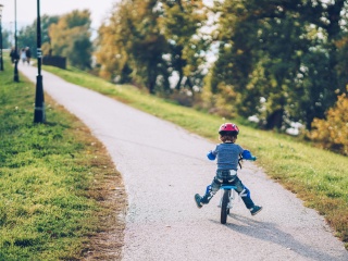 A child bikes on a path wearing a red bike helmet.