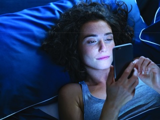 Adult woman using smartphone while in bed at night.