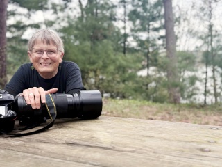 Portrait of Raven Schwan-Noble with camera in the woods.