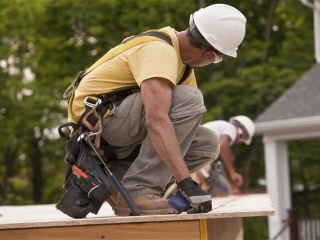 Two construction workers work on the roof of a home.