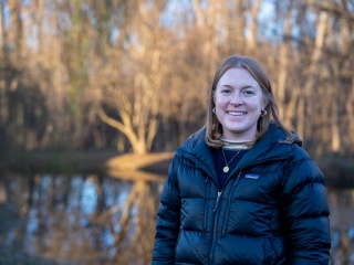Gabby Makatura poses for a photo while standing outside in a stand of trees.