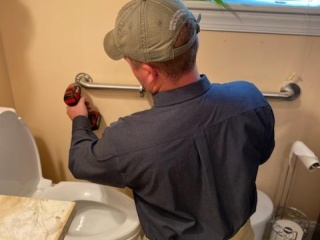 A man installs a grab bar on the wall to improve accessibility and safety.