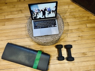 A Steps to Wellness participant uses a laptop, yoga mat and hand weights at home.