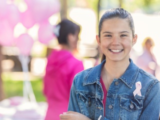 A young girl smiles wearing a breast cancer ribbon.