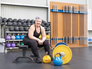 Adult woman sits on weight bench in gym during weight lifting session.