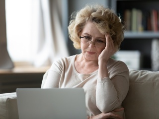 Adult woman holds forehead in frustration while using a computer.