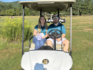 Two volunteers sit on a golf cart.