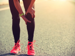 Stock photo of a runner holding their knee on a roadway.