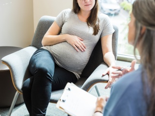 Stock photo of a pregnant woman sitting and talking to a doctor.