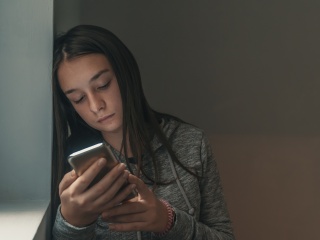 Young girl looks at cell phone in a dark room.