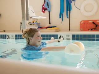 Woman doing aquatic therapy in a rehabilitation pool, holding foam resistance equipment.