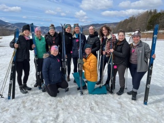 OBGYN residents pose for a group photo in the snow outdoors with their skis. 