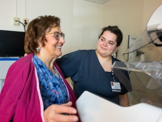 Radiology staff member assisting a patient next to a mammography machine in an imaging exam room