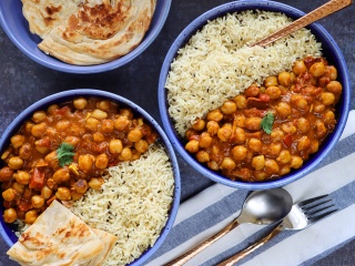 Bowls of curried chickpeas, jasmine rice and naan sit a blue table. 