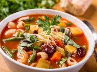 A bowl of minestrone soup sits on a table.