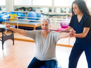A woman uses stretch bands with the help of a physical therapist during cardiac rehab.