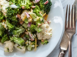 Broccoli cauliflower salad sits in a bowl next to a fork and knife.