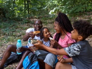 A family eats sandwiches on a camping trip hike.