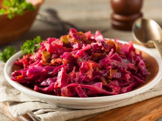 A bowl of cider braised cabbage and apples sits on a table.