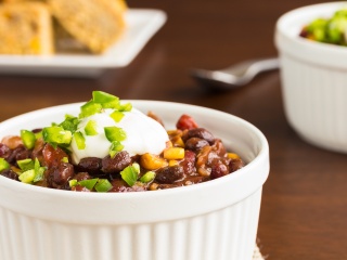Cup of slow cooker black bean chili with sour cream sits on a table.