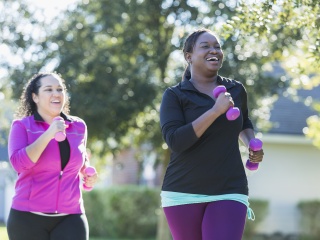 Two women walk for exercise with weights in hands.