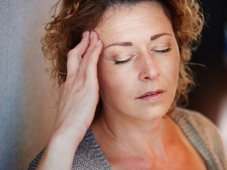 Older woman with hand to head in migraine pain.