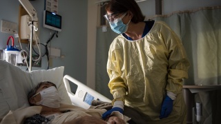 A medical provider wearing personal protective equipment checks on a patient in a hospital bed.
