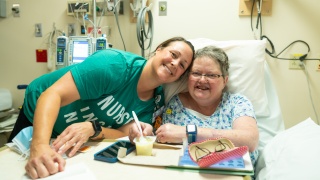Cancer support staff poses with cancer patient in hospital bed.