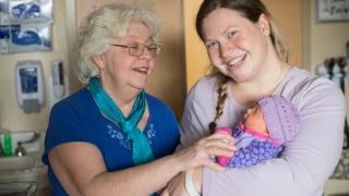 A birthing center nurse poses with a patient and her newborn baby.