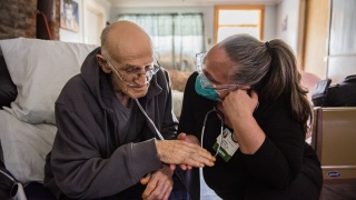 A nurse leans down and speaks to a patient sitting in a chair.