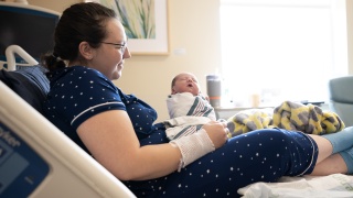 A mother reclines in a bed and holds her newborn baby.