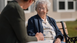 A resident of The Alice Center at Alice Hyde Medical Center chats with a staff member on a bench outdoors.