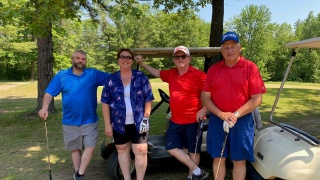 Four golfers pose in front of a golf cart.