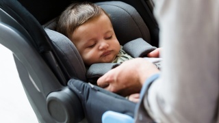 Adult buckles sleeping baby in car seat.
