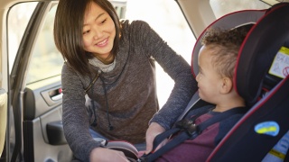 A mother buckles her child into a car seat.