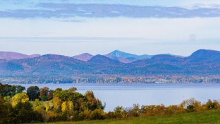 The Champlain Valley landscape and mountains sit in the distance over Lake Champlain.