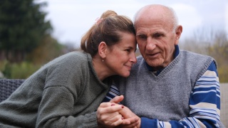 Two adults hold hands while sitting on a bench.