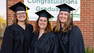 Three new nurses wearing caps and gowns smile at their graduation ceremony at Central Vermont Medical Center.